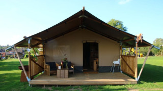Tienda safari con sanitarios, terraza de madera, zona de estar al aire libre y césped amplio alrededor.
