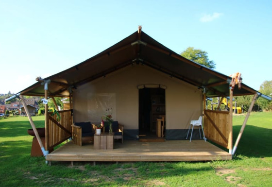 Tienda safari con sanitarios, terraza de madera, zona de estar al aire libre y césped amplio alrededor.