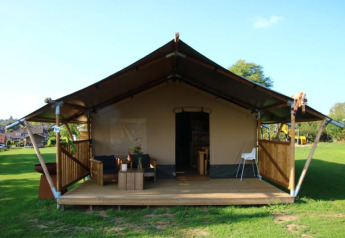 Tienda safari con sanitarios, terraza de madera, zona de estar al aire libre y césped amplio alrededor.