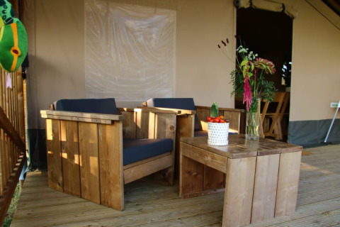 Holzmöbel und Pflanzen auf der Veranda eines Safari-Zelts bei Camping La Dolce Vita in den Niederlanden.