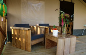 Muebles de madera y plantas en la terraza de la tienda Safari tent + sanitary en Camping La Dolce Vita, Países Bajos.