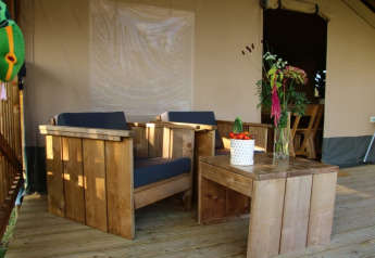 Wood furniture and plants on the veranda of Safari tent + sanitary at Camping La Dolce Vita in the Netherlands.