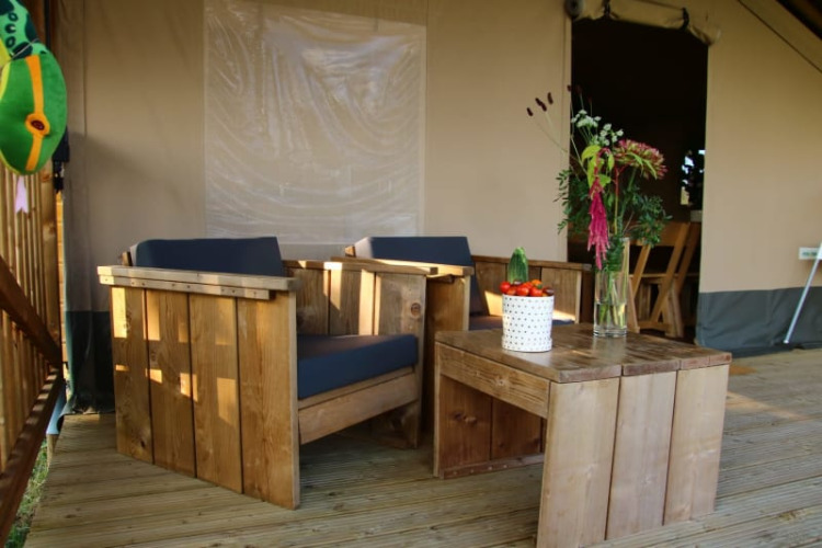 Muebles de madera y plantas en la terraza de la tienda Safari tent + sanitary en Camping La Dolce Vita, Países Bajos.