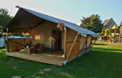Safari-Zelt mit Sanitärbereich und Holzveranda auf Camping La Dolce Vita in den Niederlanden, Spielplatz im Hintergrund.
