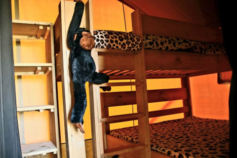 Interior de tienda safari con literas, ropa de cama de leopardo y mono de peluche en Camping La Dolce Vita.