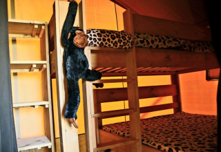 Interior de tienda safari con literas, ropa de cama de leopardo y mono de peluche en Camping La Dolce Vita.