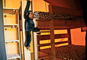 Interior de tienda safari con literas, ropa de cama de leopardo y mono de peluche en Camping La Dolce Vita.
