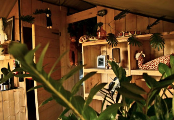 Interior view of a safari tent with wooden walls, jungle-themed plush toys, and green plants in the Netherlands.