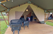 Tienda safari en Camping Yttermalungs, Suecia, con terraza de madera, sillas plásticas y luz interior.