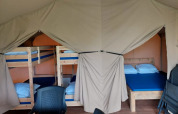 Interior de tienda safari en Camping Yttermalungs, Suecia, con literas, cama doble y sillas de plástico.