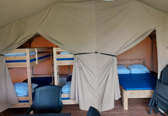 Interno della tenda safari al Camping Yttermalungs in Svezia con letti a castello, letto matrimoniale e sedie.