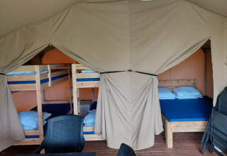 Interior de tienda safari en Camping Yttermalungs, Suecia, con literas, cama doble y sillas de plástico.