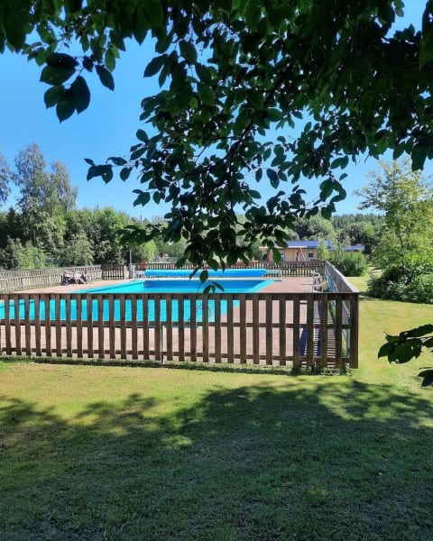 View of a fenced swimming pool with green lawn and trees at Safari tent, Camping Yttermalungs, Sweden.