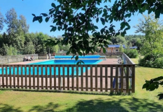 View of a fenced swimming pool with green lawn and trees at Safari tent, Camping Yttermalungs, Sweden.