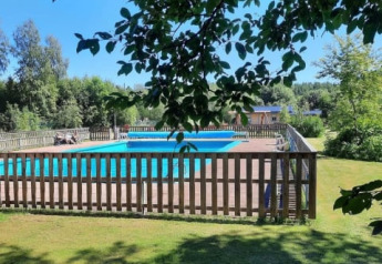View of a fenced swimming pool with green lawn and trees at Safari tent, Camping Yttermalungs, Sweden.