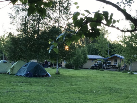 Safari tent at Camping Yttermalungs in Sweden with green grass, tents, cabins, and vintage cars at sunset.
