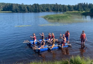 Bambini e adulti remano su una zattera fatta in casa presso la tenda safari al Camping Yttermalungs, Svezia.