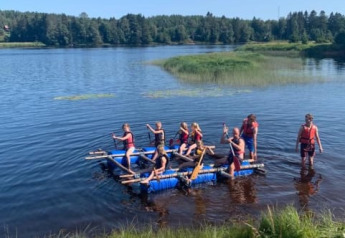 Niños y adultos reman en una balsa casera en un lago junto a la tienda safari en Camping Yttermalungs, Suecia.