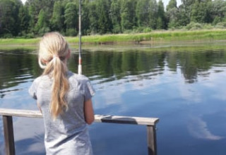 Niña pescando desde un muelle de madera junto al lago en Safari tent de Camping Yttermalungs, Suecia, en verano.