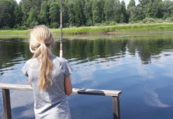 Bambina che pesca da un molo di legno presso il lago vicino a Safari tent al Camping Yttermalungs, Svezia.