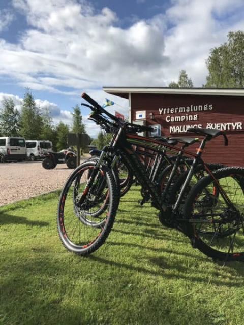 Several mountain bikes are parked on grass near the safari tent at Camping Yttermalungs, Sweden, sunny day.