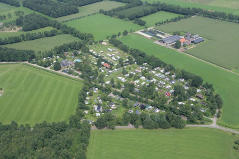 Vue aérienne d’un camping avec tentes safari, entouré de champs verts et d’arbres à la campagne.