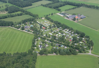 Aerial view of a campsite with safari tents, surrounded by green fields and trees in the countryside.