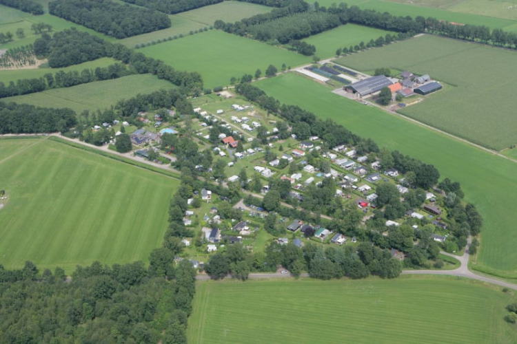 Vista aérea de un campamento con tiendas safari, rodeado de campos verdes y bosques en el campo.