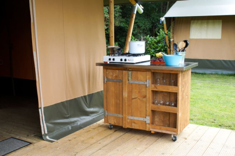 Udendørs køkken på hjul ved en safaritelts terrasse på Camping de Meibeek, Holland, med gaskomfur og skåle.