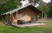 Safari-Zelt mit Sanitäreinrichtungen, Terrasse mit Stühlen, Fahrrädern und grünem, bewaldetem Umfeld.