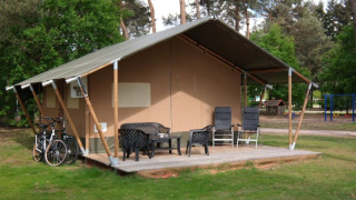 Tienda safari con baño privado, terraza con sillas, bicicletas y entorno verde con árboles y parque.