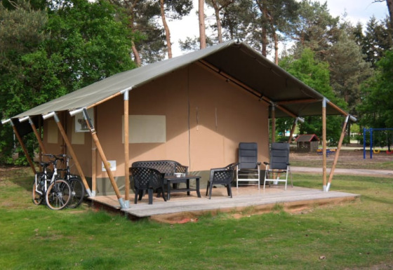 Tienda safari con baño privado, terraza con sillas, bicicletas y entorno verde con árboles y parque.