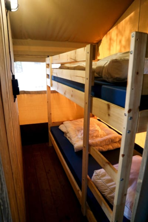 Intérieur d'une tente safari avec lits superposés en bois, matelas bleus et lumière chaleureuse.