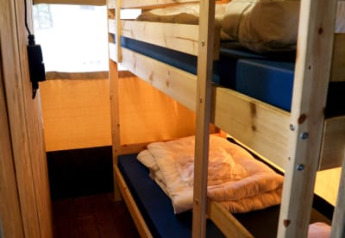 Interior de una tienda safari con literas de madera, colchones azules, ropa de cama y luz cálida.