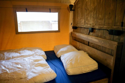 Vista interior de Safari tent + sanitary en Camping de Meibeek, Países Bajos, con cama y pared de madera.