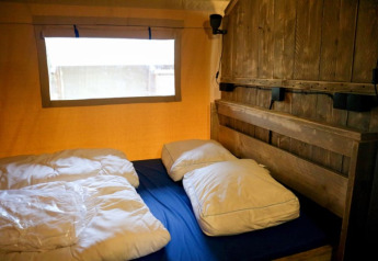 Vista interior de Safari tent + sanitary en Camping de Meibeek, Países Bajos, con cama y pared de madera.