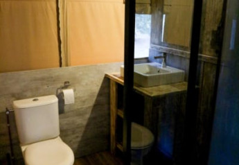 Baño moderno en tienda safari con inodoro, lavabo, ducha acristalada y paredes y suelos tipo madera.