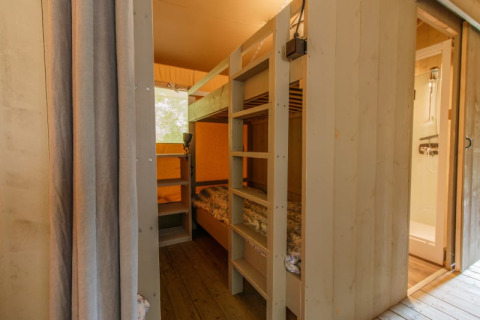 Interior de una tienda safari con literas y baño privado, paredes de madera y una decoración acogedora.