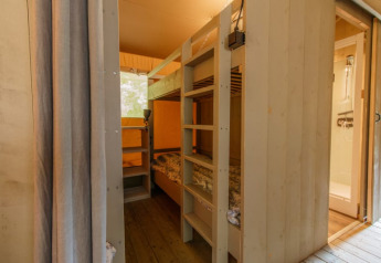 Interno di tenda safari con letti a castello e bagno privato, pareti in legno e atmosfera accogliente.