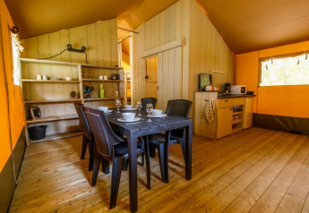 Interieur van een safaritent met eettafel, zwarte stoelen, keuken en houten vloer voor glamping.