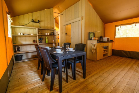 Interior de tienda safari con mesa de comedor, sillas negras, cocina y suelo de madera clara.