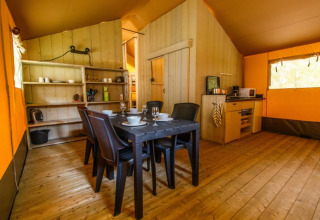 Innenansicht eines Safari-Zelts mit Esstisch, Kunststoffstühlen, Küche und Holzboden.