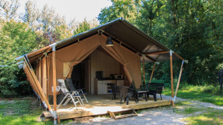 Tenda safari con servizi igienici privati, area relax esterna e verde bosco tutto attorno.