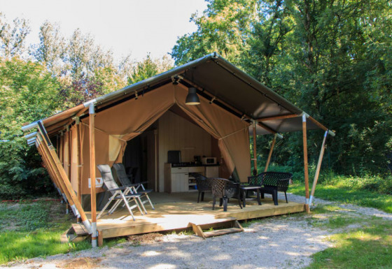 Tienda safari con baño privado, zona de asientos al aire libre y rodeada de bosque verde.