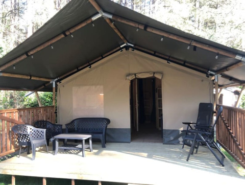 Safari tent + sanitary with covered wooden deck, outdoor seating area, and forest surroundings shown.