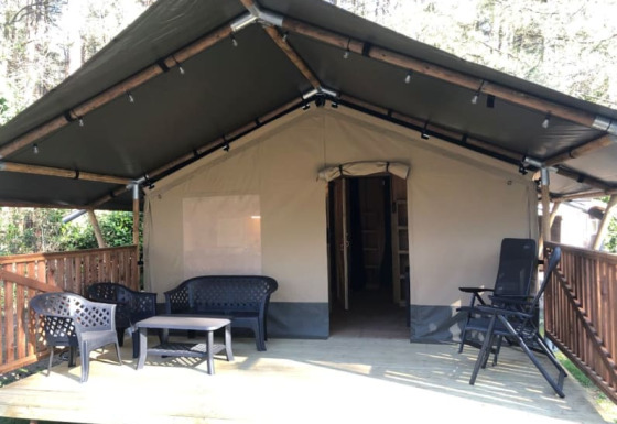 Tienda safari + sanitario con terraza cubierta de madera y zona de estar al aire libre en la naturaleza.