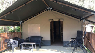 Tienda safari + sanitario con terraza cubierta de madera y zona de estar al aire libre en la naturaleza.