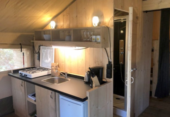 Keuken in safaritent met gaskookplaat, gootsteen, koelkast en badkamer bij Camping Siësta in België.