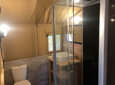 Baño moderno dentro de una tienda safari en Camping Siësta, Bélgica, con ducha, inodoro y lavabo.
