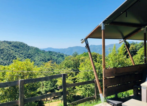 Blick von einer Safari-Zelt-Terrasse auf grüne Hügel unter blauem Himmel, perfekt zum Entspannen.